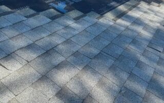 Partially completed roof installation showing Timberline HD shingles being laid over synthetic underlayment, with roofing materials visible on the upper section.