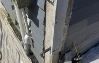 Close-up of a house corner showing decayed and rotting wood trim being removed, with a power saw and tools on a drop cloth during siding repair work.